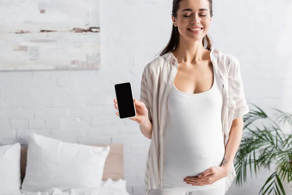 Довольная и беременная женщина держит смартфон с чистым экраном — стоковое фото