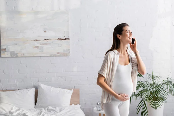 Femme enceinte positive parlant sur smartphone dans la chambre — Photo de stock