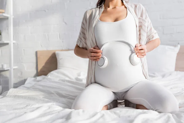 Vue recadrée d'une jeune femme enceinte tenant un casque près du ventre — Photo de stock