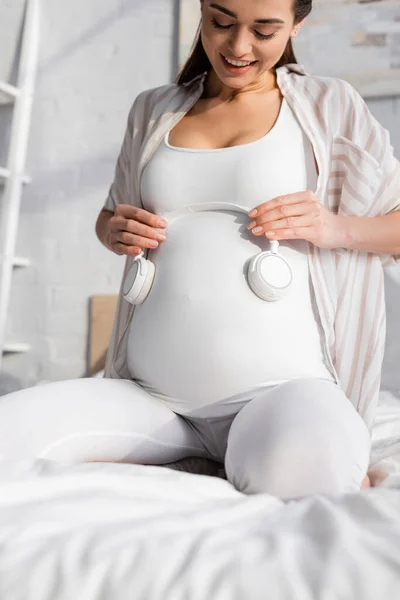 Позитивна вагітна жінка тримає бездротові навушники біля живота — стокове фото