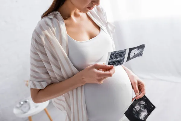 Vista parcial de la mujer embarazada sosteniendo fotos de ultrasonido - foto de stock