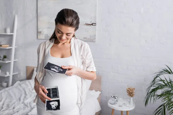 Mujer embarazada complacida sosteniendo ecografías - foto de stock