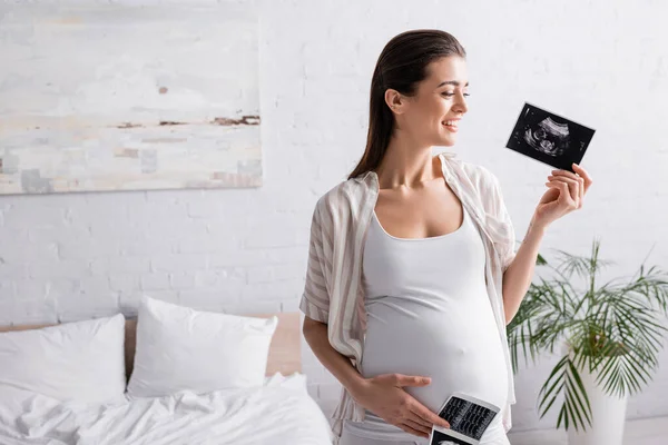 Mujer sonriente y embarazada sosteniendo ecografías - foto de stock
