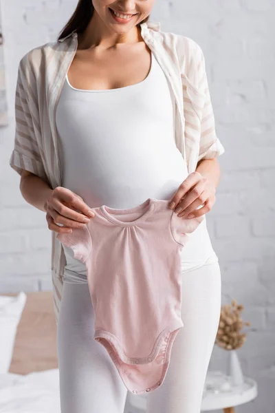 Частковий вигляд задоволеної вагітної жінки, що тримає рожевий дитячий рум'янець у спальні — стокове фото