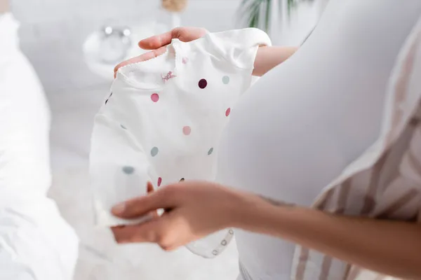 Vista cortada de mulher grávida borrada segurando bebê romper no quarto — Fotografia de Stock