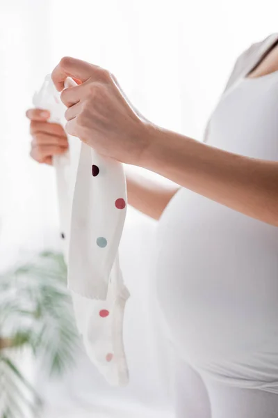 Partial view of pregnant woman holding baby romper in bedroom — Stock Photo