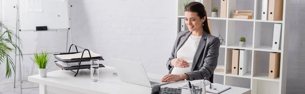 Happy pregnant businesswoman looking at laptop in office, banner — Stock Photo