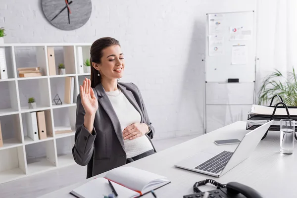 Happy pregnant businesswoman waving hand during video call tattoo — Stock Photo