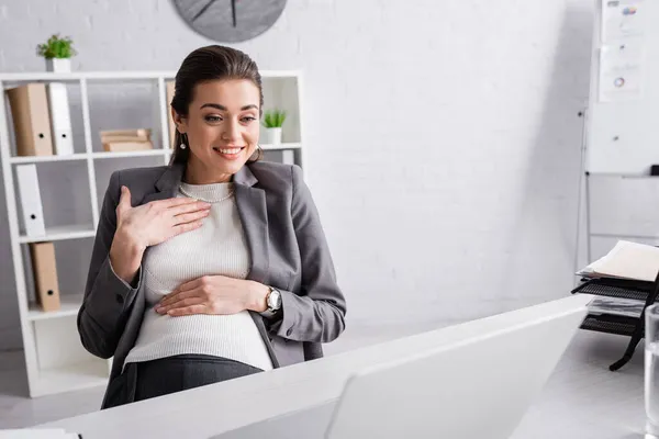 Счастливая беременная деловая женщина улыбается во время видеозвонка — стоковое фото