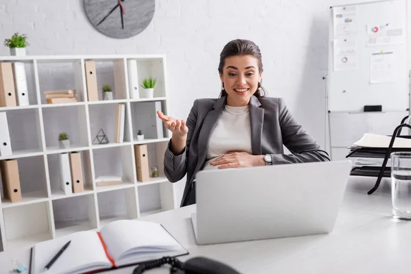 Fröhliche schwangere Geschäftsfrau gestikuliert in der Nähe von Laptop im Büro — Stockfoto