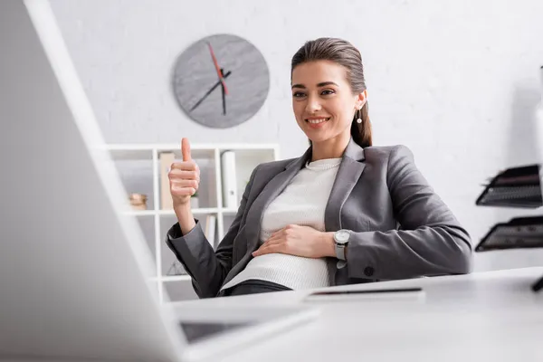 Feliz embarazada mujer de negocios mostrando pulgar hacia arriba durante la videollamada en el ordenador portátil - foto de stock
