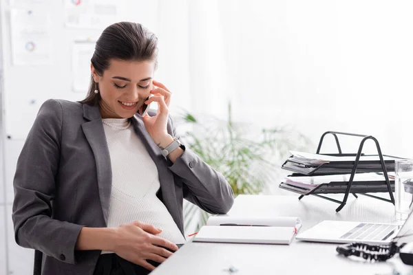 Femme d'affaires enceinte positive parlant sur smartphone au bureau — Photo de stock