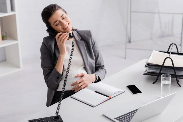 Счастливая беременная деловая женщина разговаривает по ретро телефону — стоковое фото