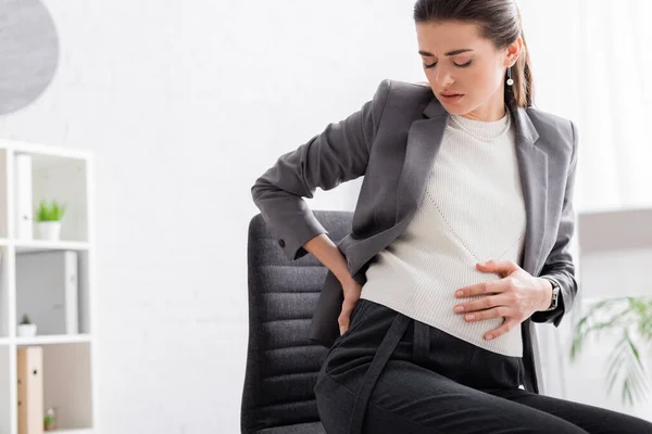 Exhausted pregnant woman touching belly in office — Stock Photo