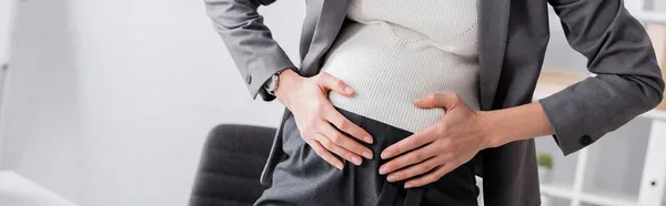 Abgeschnittene Ansicht einer jungen schwangeren Geschäftsfrau, die Bauch berührt, während sie Krämpfe verspürt, Banner — Stockfoto