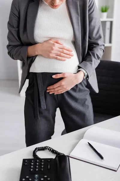 Cropped view of young pregnant businesswoman touching belly while feeling cramp — Stock Photo