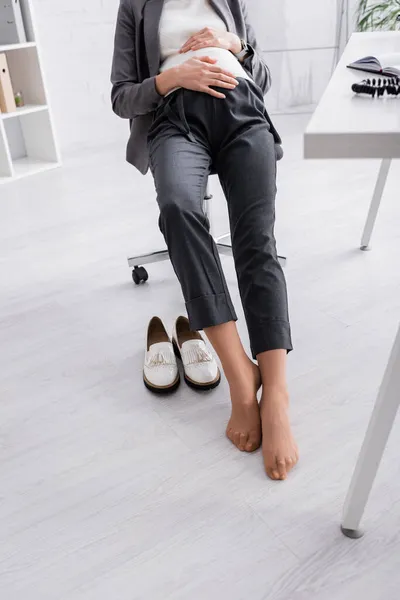 Vue partielle de la femme enceinte sans chaussure assise sur la chaise dans le bureau — Photo de stock