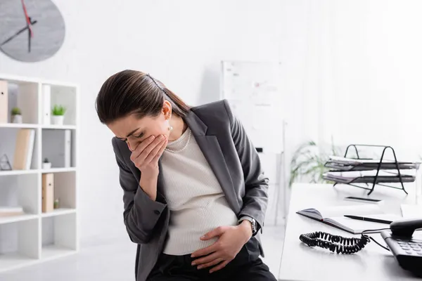 Pregnant businesswoman feeling nausea and covering mouth — Stock Photo