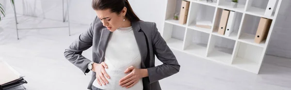 Hochwinkelaufnahme einer unzufriedenen schwangeren Geschäftsfrau, die Bauch berührt, während sie Krämpfe verspürt, Banner — Stockfoto