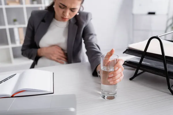 Blurred pregnant businesswoman feeling cramp and reaching glass of water — Stock Photo