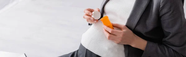 Vista ritagliata della donna incinta che tiene il vaso con le pillole in ufficio, banner — Foto stock