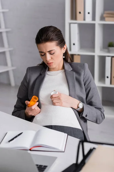 Femme enceinte tenant pot avec des pilules au bureau — Photo de stock