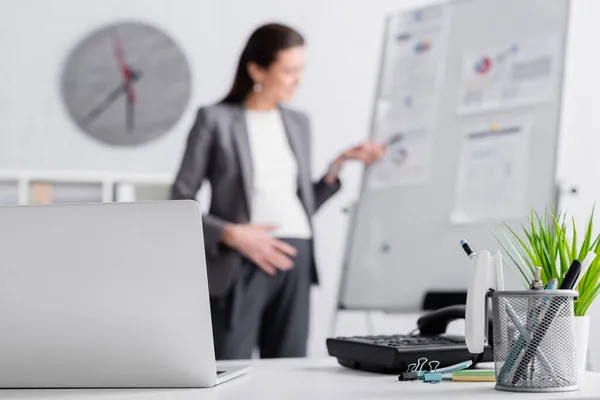 Laptop perto de mulher de negócios grávida perto de flip chart no fundo borrado — Fotografia de Stock