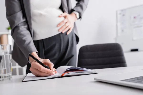 Ausgeschnittene Ansicht einer schwangeren Geschäftsfrau, die in Notizbuch schreibt — Stockfoto