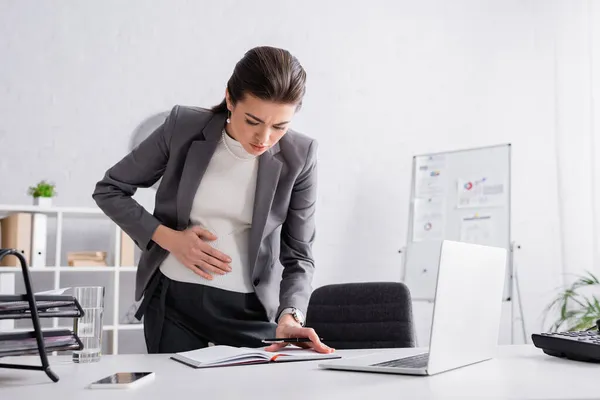 Empresaria embarazada escribiendo en cuaderno cerca de gadgets en la mesa - foto de stock