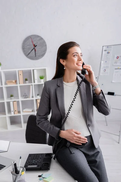 Happy pregnant businesswoman talking on retro telephone in office — Stock Photo