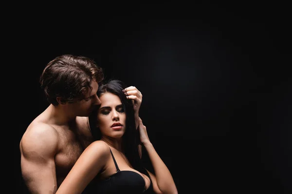 Apasionado hombre oliendo pelo de morena mujer en sujetador aislado en negro - foto de stock