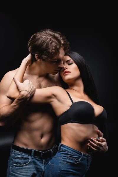 Brunette woman in bra hugging shirtless boyfriend on black — Stock Photo