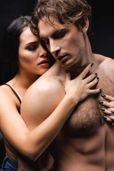 Brunette woman touching chest of shirtless boyfriend isolated on black — Stock Photo