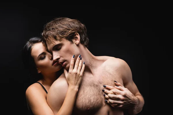 Brunette woman touching face of shirtless boyfriend isolated on black — Stock Photo