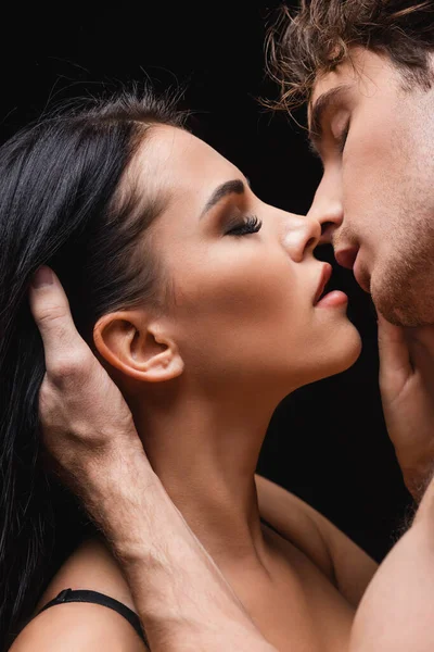 Vista lateral de pareja apasionada con los ojos cerrados besándose aislado en negro - foto de stock