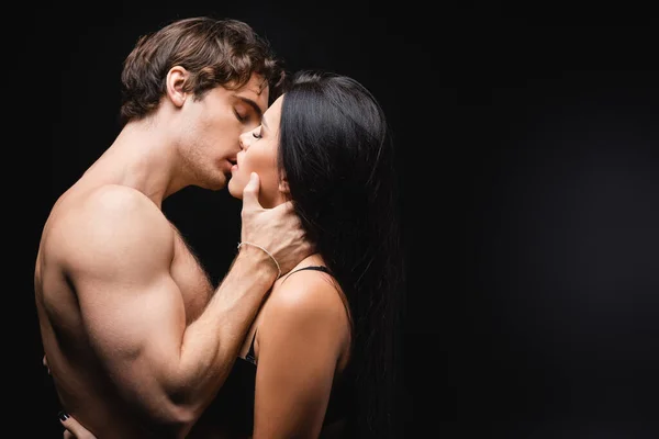 Vista lateral de jovem e sexy casal com olhos fechados beijando no preto — Fotografia de Stock