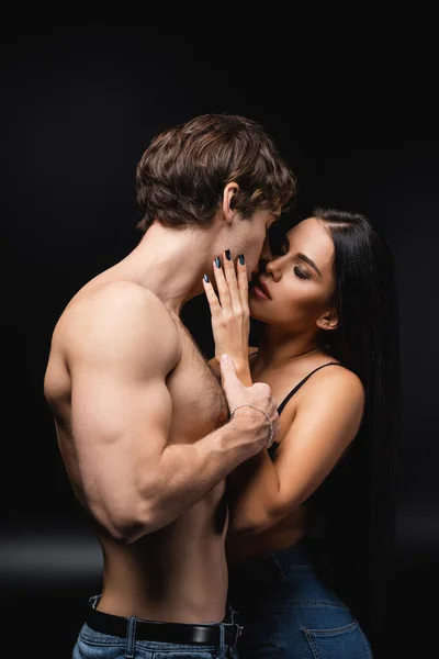 Young woman in bra hugging and kissing muscular boyfriend on black — Stock Photo