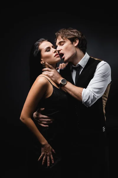 Passionate man with open mouth hugging seductive girlfriend in slip dress isolated on black — Stock Photo