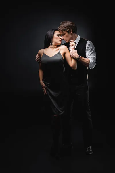 Longitud completa del hombre en chaleco y camisa abrazando novia en vestido de deslizamiento sexy en negro - foto de stock