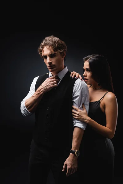 Молодая сексуальная женщина в платье обнимает мужчину в жилете и рубашке на черном — стоковое фото