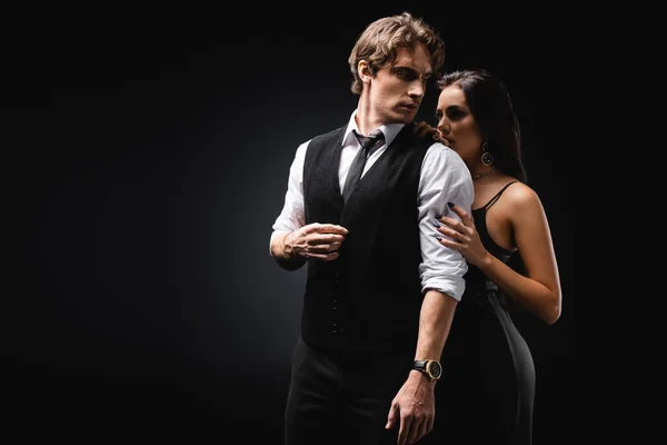 Mujer sexy en vestido de deslizamiento abrazando al hombre en chaleco y camisa en negro - foto de stock