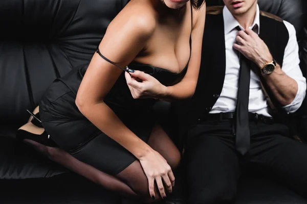 Alta vista angular de la mujer ajustando la correa en vestido de seda cerca de novio apasionado sentado en el sofá - foto de stock