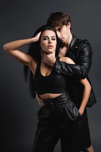 Man in leather jacket hugging sexy woman in black crop top on grey — Stock Photo