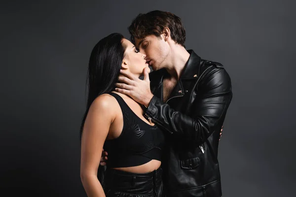 Man in leather jacket kissing sexy woman in black crop top on grey — Stock Photo