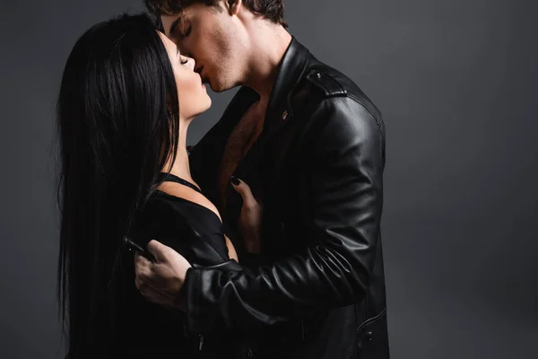 Сексуальна молода пара в шкіряних куртках цілується на сірому — стокове фото