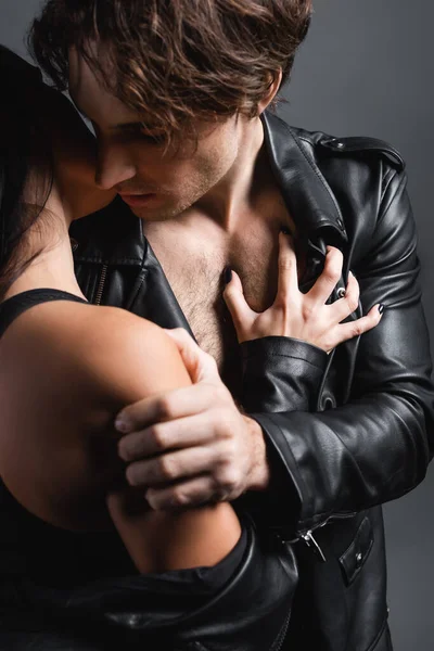 Donna appassionata gratta e vinci petto del fidanzato in giacca di pelle isolata su grigio — Foto stock
