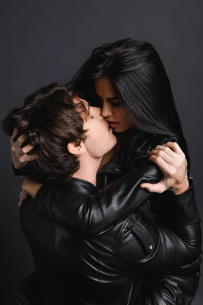 Joven apasionado hombre y sexy mujer en cuero chaqueta besos aislado en gris - foto de stock