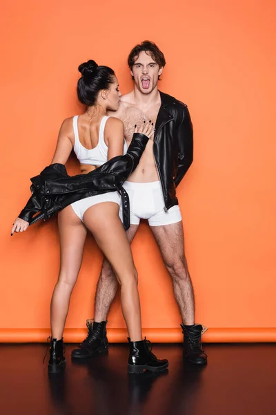 Full length of man sticking out tongue while standing with sexy woman in black leather jacket on orange — Stock Photo