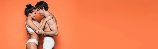 Happy and sexy couple in white underwear hugging on orange, banner — Stock Photo