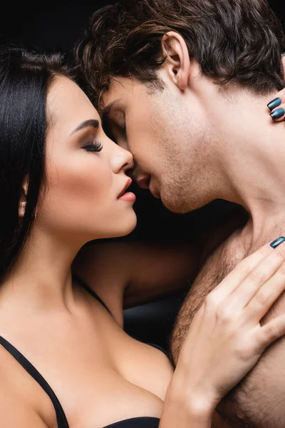 Vista lateral de pareja joven abrazándose mientras se besa en negro - foto de stock